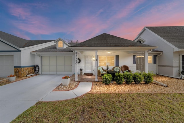 single story home with roof with shingles, covered porch, concrete driveway, an attached garage, and ceiling fan