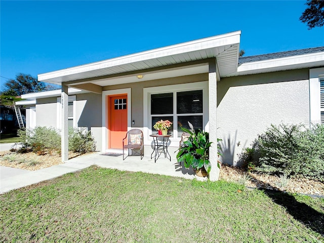 property entrance featuring a porch, a lawn, and stucco siding