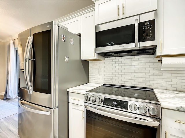 kitchen with light stone counters, light wood-style flooring, white cabinets, appliances with stainless steel finishes, and decorative backsplash