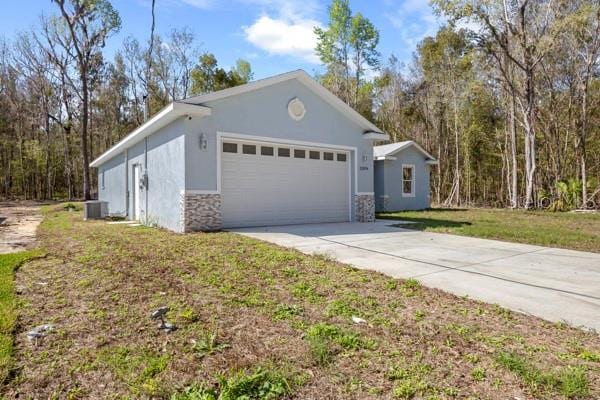 view of front of home featuring stucco siding, central AC unit, a garage, stone siding, and driveway