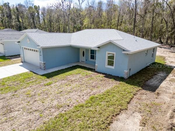 ranch-style house with concrete driveway, a forest view, an attached garage, and stucco siding