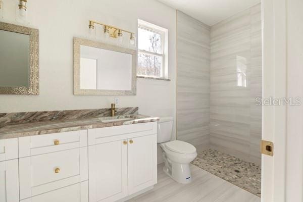 bathroom featuring a tile shower, vanity, and toilet