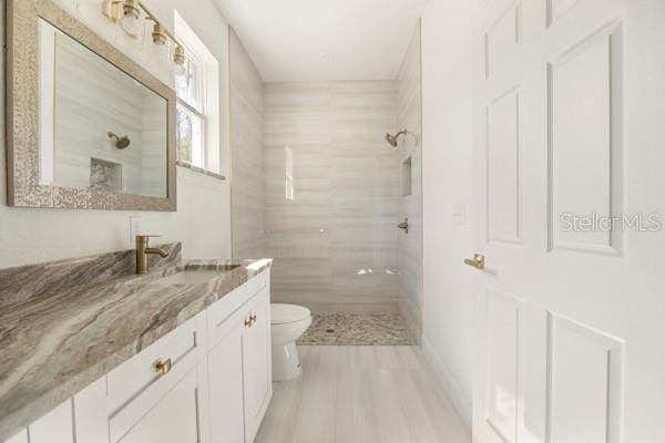 full bath featuring tiled shower, vanity, and toilet