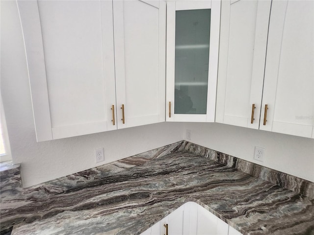 room details with dark stone countertops, glass insert cabinets, and white cabinets