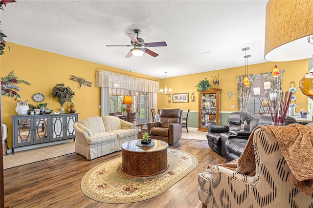 living area featuring ceiling fan with notable chandelier, a textured ceiling, and wood finished floors