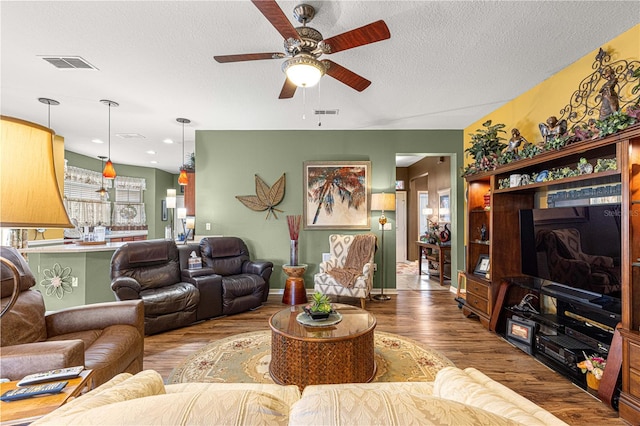 living room featuring a ceiling fan, a textured ceiling, visible vents, and wood finished floors