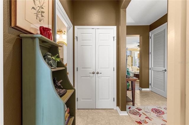 interior space featuring light tile patterned floors, a textured wall, and baseboards