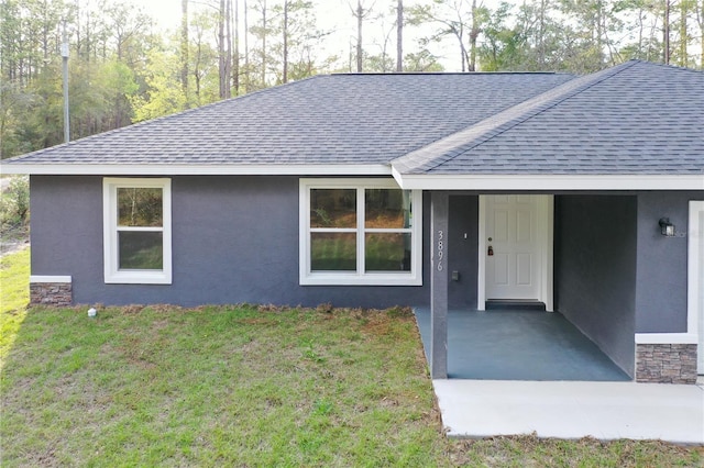 view of front facade with a shingled roof, a front yard, and stucco siding