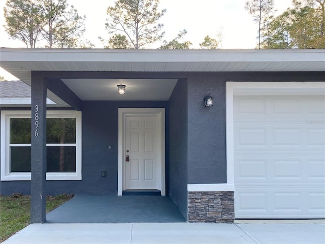 entrance to property featuring a garage, stone siding, and stucco siding