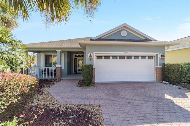 single story home featuring a porch, an attached garage, brick siding, decorative driveway, and stucco siding