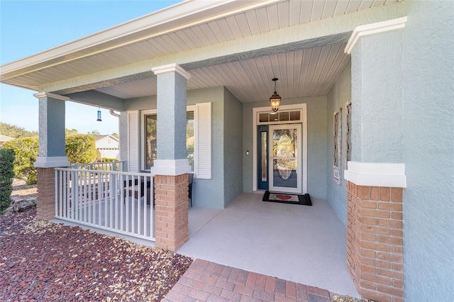 property entrance featuring a porch, brick siding, and stucco siding