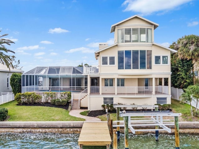 back of property with boat lift, stucco siding, a water view, a lawn, and fence