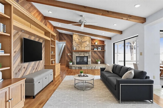 living area with light wood finished floors, built in shelves, a stone fireplace, and beam ceiling