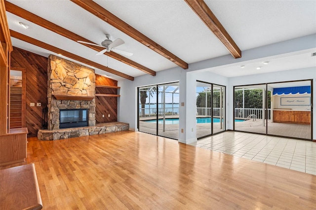 unfurnished living room featuring a stone fireplace, wood walls, wood finished floors, baseboards, and beam ceiling