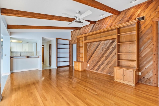 unfurnished living room with light wood-type flooring, visible vents, vaulted ceiling with beams, and wooden walls