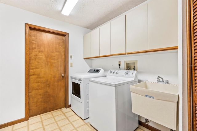 clothes washing area with cabinet space, a textured ceiling, washer and dryer, light floors, and a sink