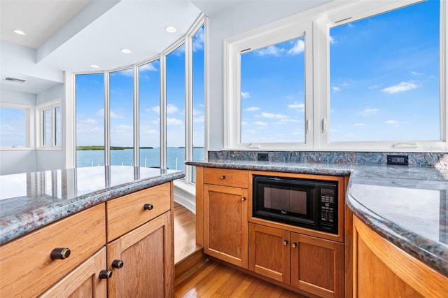 kitchen featuring black microwave, a water view, visible vents, light wood finished floors, and dark stone countertops