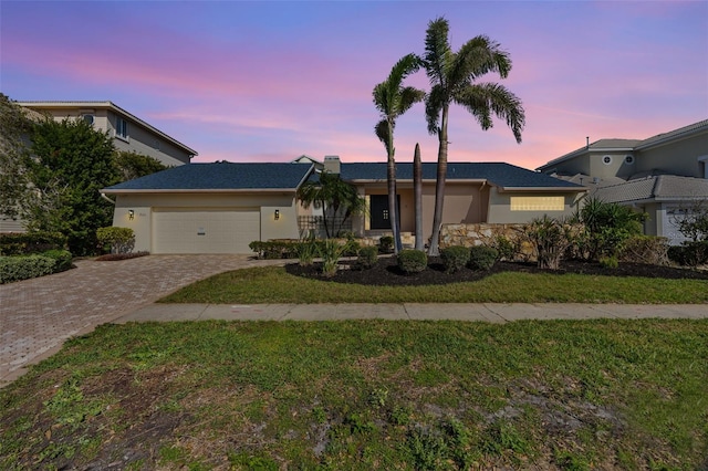 single story home featuring a yard, decorative driveway, an attached garage, and stucco siding