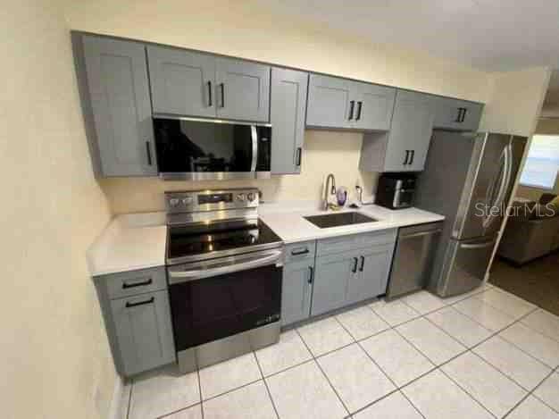 kitchen featuring gray cabinets, stainless steel appliances, a sink, and light countertops