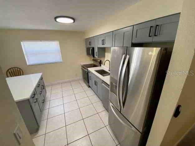 kitchen featuring light tile patterned floors, stainless steel appliances, light countertops, gray cabinetry, and a sink