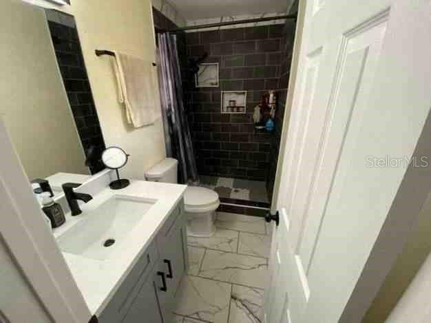 full bath with marble finish floor, a stall shower, vanity, and toilet