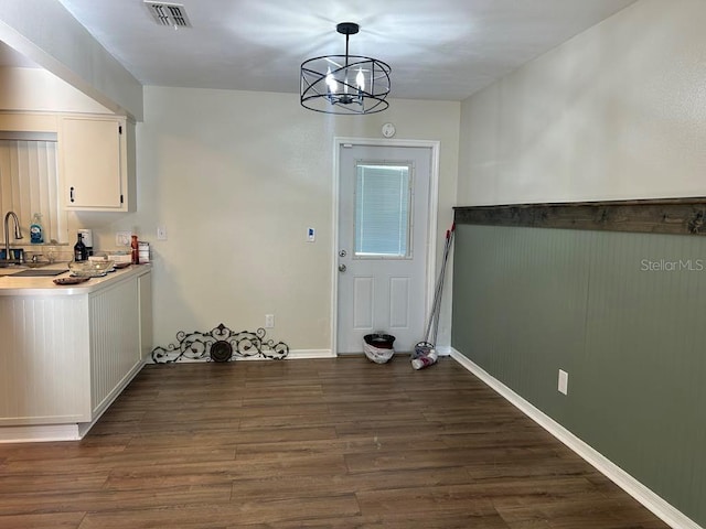 unfurnished dining area with baseboards, visible vents, dark wood-style flooring, a notable chandelier, and a sink