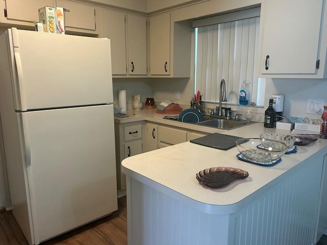 kitchen featuring a peninsula, a sink, light countertops, freestanding refrigerator, and dark wood finished floors