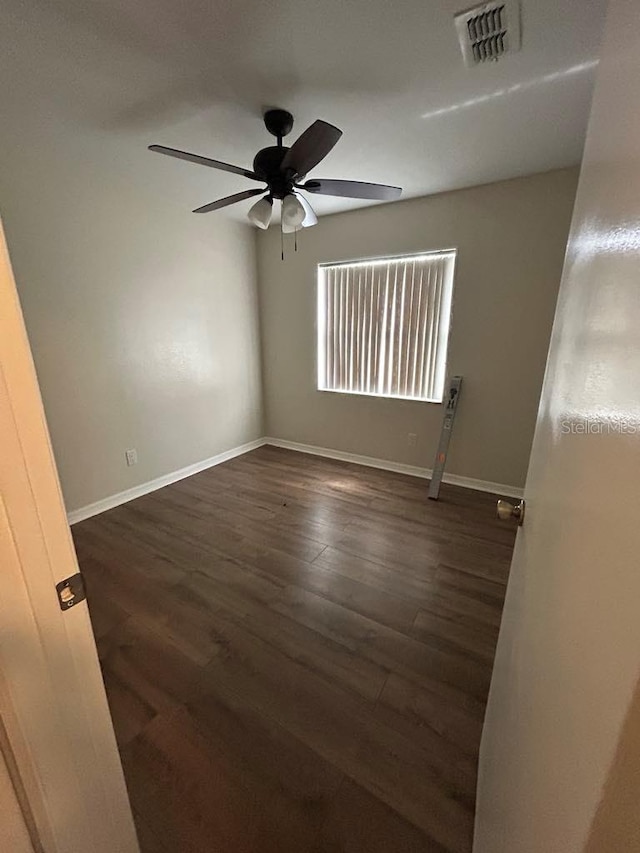 spare room featuring a ceiling fan, dark wood finished floors, visible vents, and baseboards