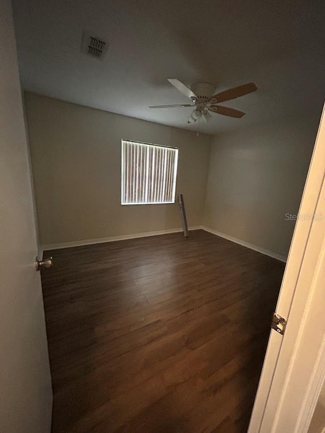 spare room featuring ceiling fan, dark wood-type flooring, visible vents, and baseboards