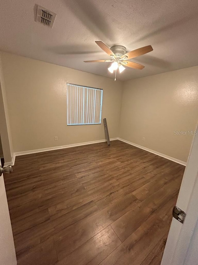 spare room featuring baseboards, visible vents, a ceiling fan, dark wood-type flooring, and a textured ceiling