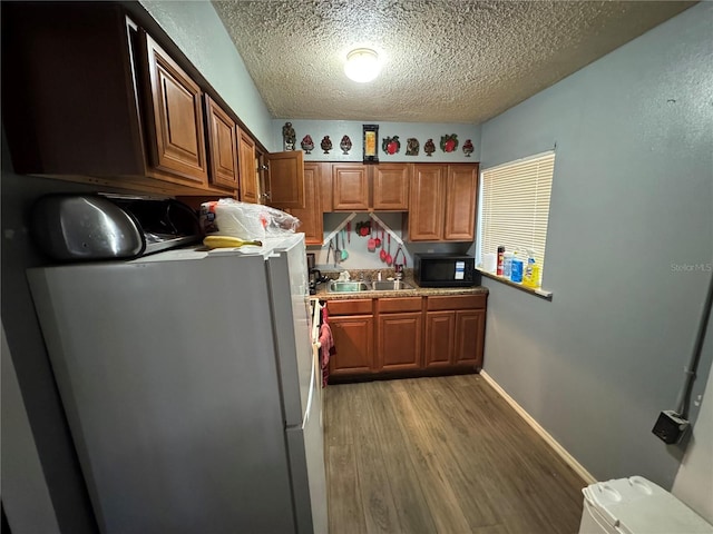 1622 NW 16th St, Ocala, FL 34475 - kitchen featuring light wood-style flooring, a textured ceiling, freestanding refrigerator, black microwave, and baseboards