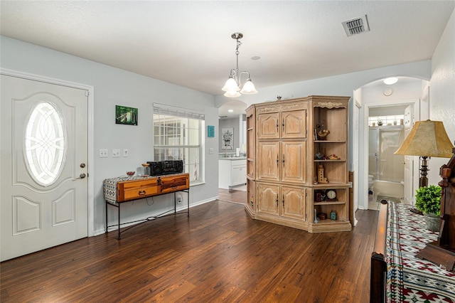 foyer entrance featuring arched walkways, a notable chandelier, visible vents, dark wood-type flooring, and baseboards