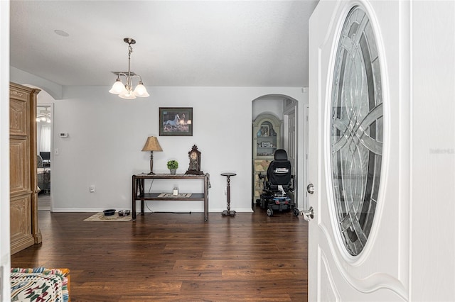 foyer entrance with dark wood-style floors, arched walkways, a chandelier, and baseboards