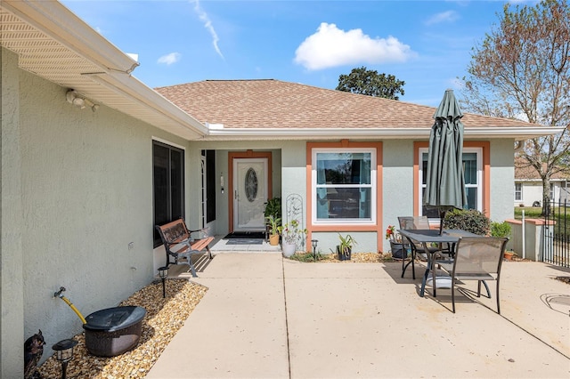 property entrance featuring roof with shingles, a patio area, fence, and stucco siding