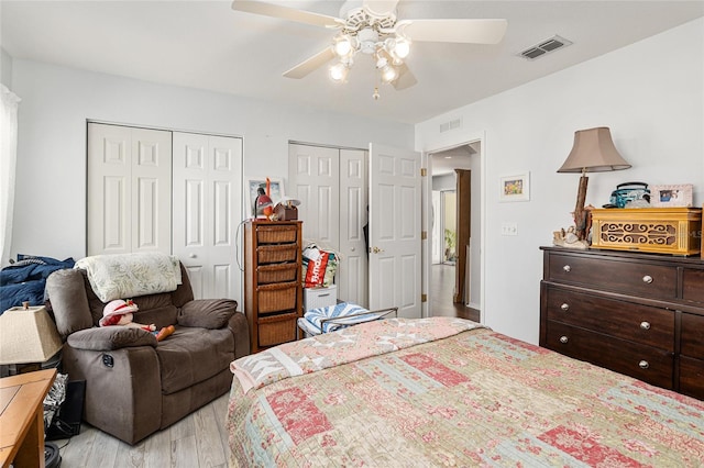 bedroom featuring visible vents, ceiling fan, light wood-style flooring, and two closets