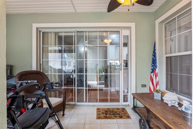 doorway with ceiling fan, a textured wall, and tile patterned flooring