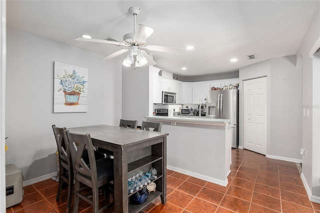 kitchen featuring white cabinets, stainless steel appliances, a ceiling fan, and dark tile patterned flooring