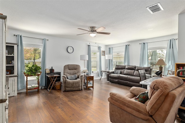 living area featuring a ceiling fan, a textured ceiling, visible vents, and dark wood-style flooring