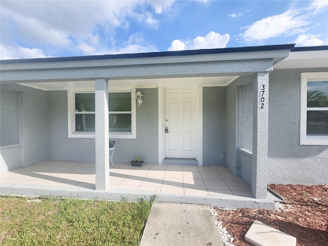 doorway to property with covered porch and stucco siding