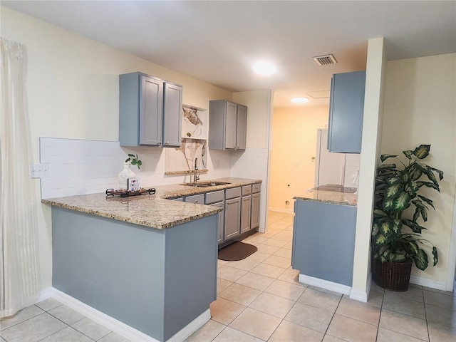 kitchen featuring a peninsula, gray cabinets, a sink, and light stone countertops