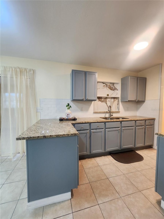 kitchen with a peninsula, backsplash, a sink, and gray cabinetry