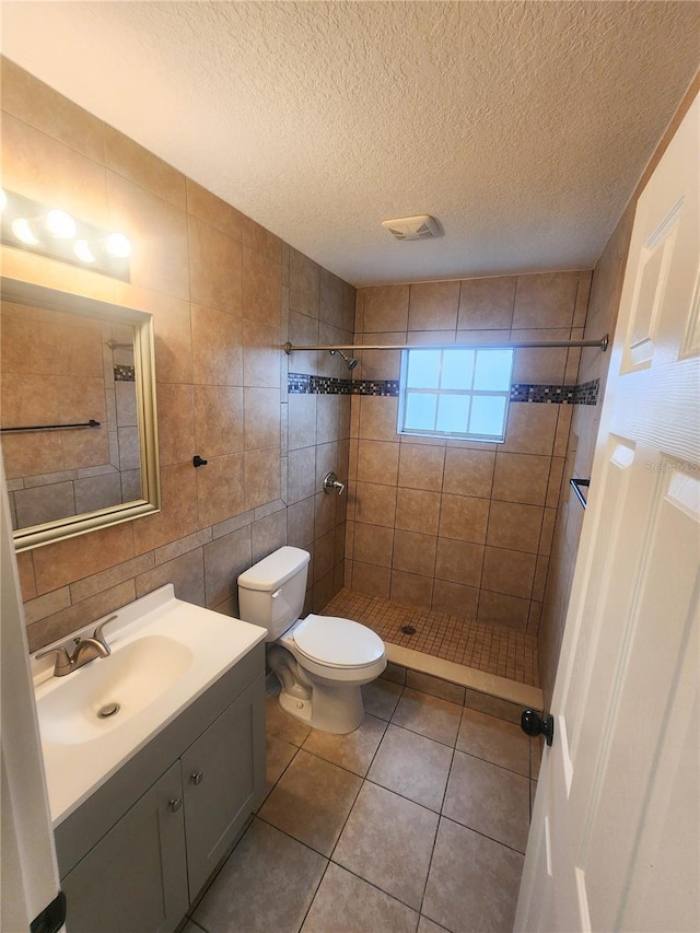 bathroom with tile walls, toilet, a tile shower, vanity, and tile patterned flooring