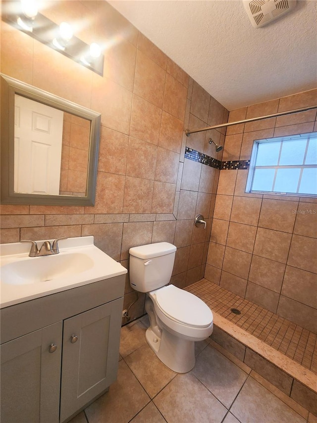 bathroom featuring toilet, vanity, visible vents, tile walls, and a tile shower