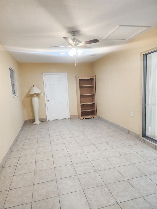 empty room featuring attic access, a ceiling fan, baseboards, and light tile patterned floors