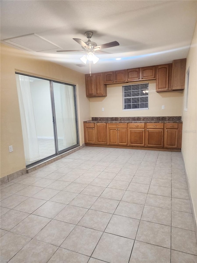 kitchen featuring light tile patterned floors, baseboards, a ceiling fan, and brown cabinets