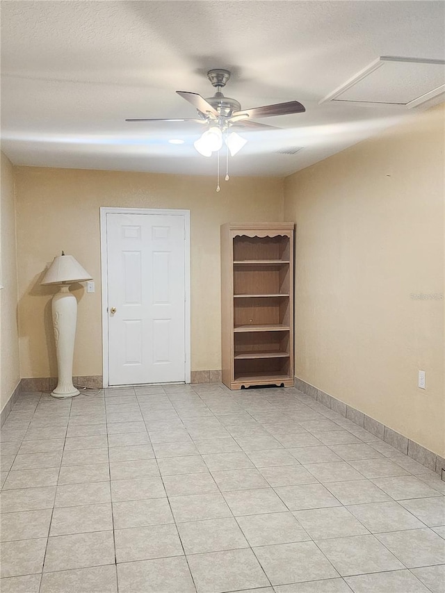 spare room with ceiling fan, a textured ceiling, baseboards, and light tile patterned floors