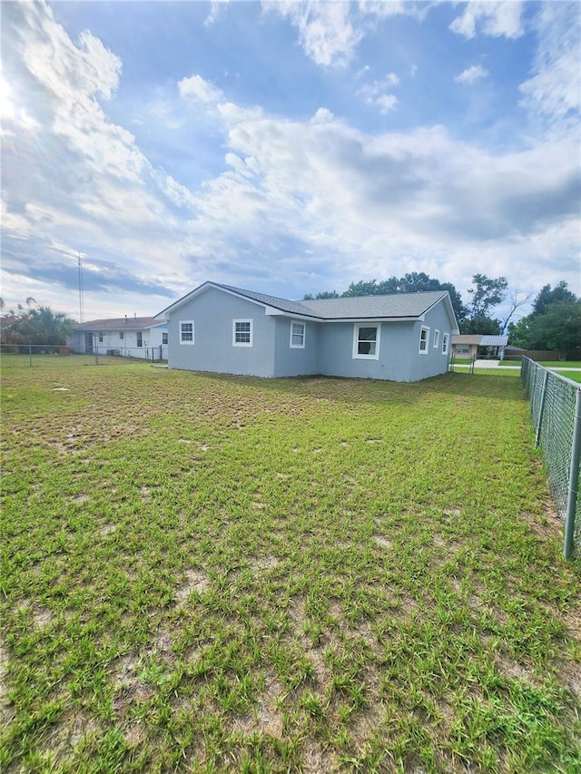 back of property with stucco siding, a lawn, and fence