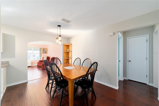 dining room featuring dark wood-style floors, a textured ceiling, arched walkways, and visible vents