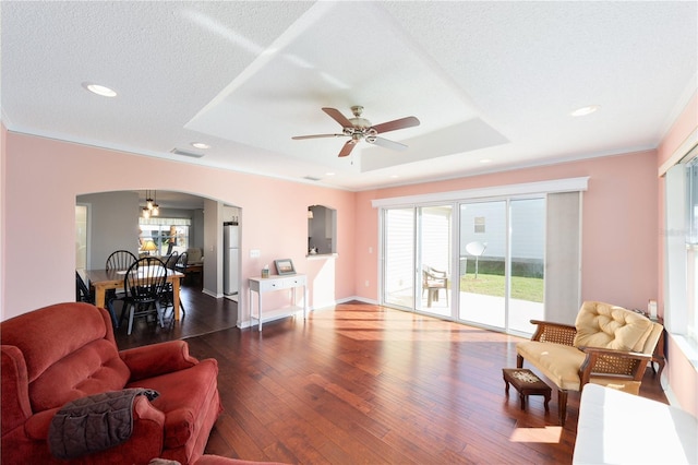 living area featuring arched walkways, a tray ceiling, dark wood-type flooring, and visible vents