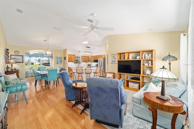 living area with vaulted ceiling, light wood-type flooring, and ceiling fan